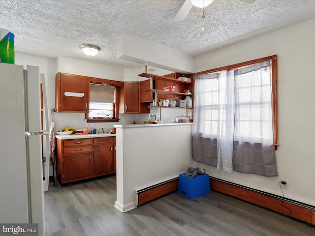 kitchen featuring white fridge, baseboard heating, and light hardwood / wood-style flooring