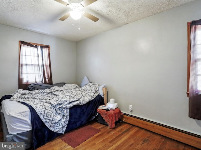 bedroom with ceiling fan, a baseboard radiator, wood-type flooring, and a textured ceiling