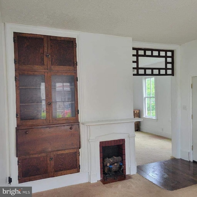 unfurnished living room featuring carpet flooring, radiator, a brick fireplace, and a textured ceiling