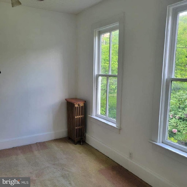 unfurnished room with a healthy amount of sunlight, radiator heating unit, and light colored carpet