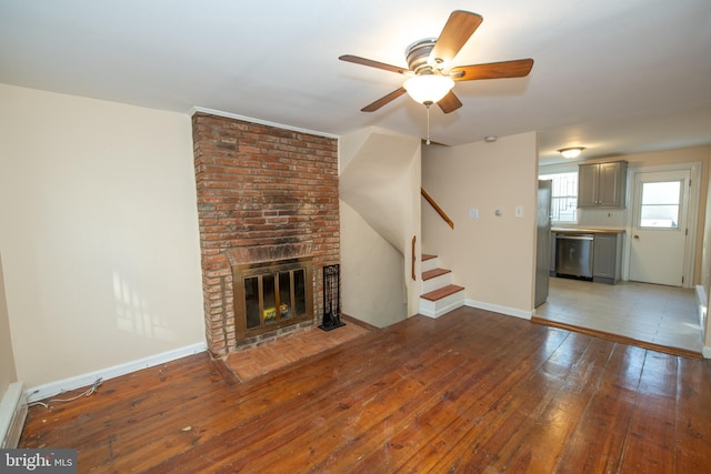 unfurnished living room featuring a brick fireplace, wood-type flooring, and ceiling fan