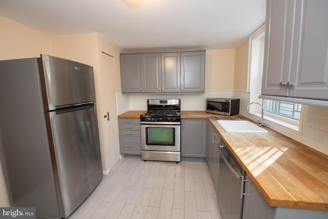 kitchen featuring appliances with stainless steel finishes, tasteful backsplash, butcher block counters, sink, and gray cabinetry