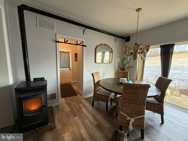 dining space with an inviting chandelier, wood-type flooring, and a wood stove