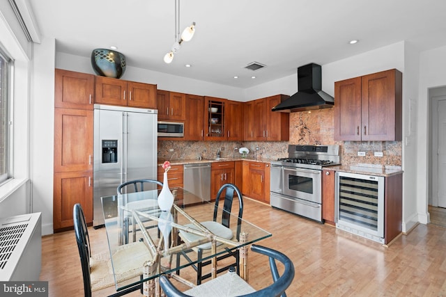 kitchen with hanging light fixtures, appliances with stainless steel finishes, wall chimney range hood, beverage cooler, and backsplash