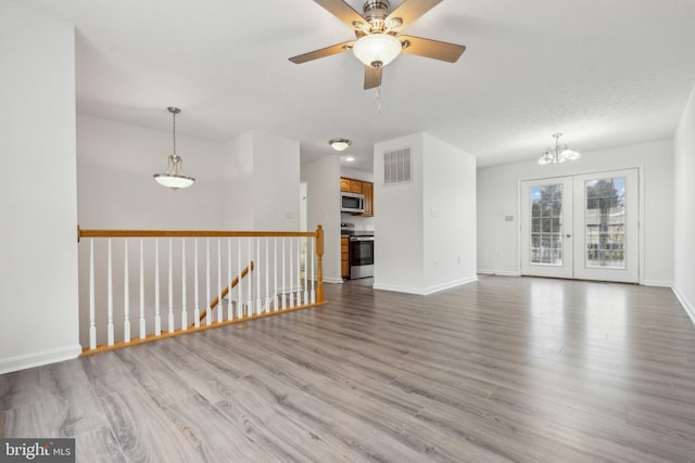 unfurnished living room featuring ceiling fan with notable chandelier, french doors, and light wood-type flooring