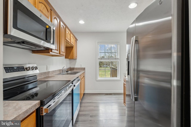 kitchen with sink, light hardwood / wood-style flooring, stainless steel appliances, and a textured ceiling