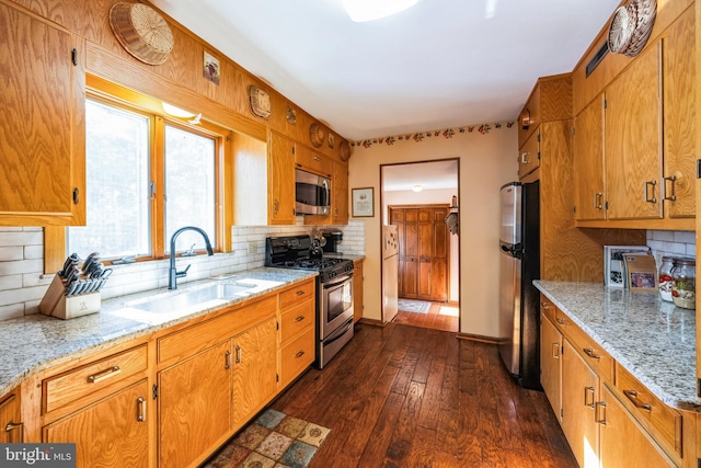 kitchen with sink, backsplash, stainless steel appliances, light stone counters, and dark hardwood / wood-style flooring