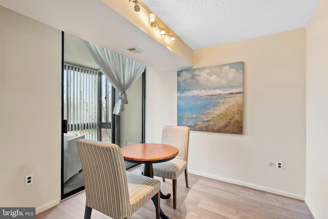 dining area with rail lighting, a textured ceiling, and light hardwood / wood-style floors