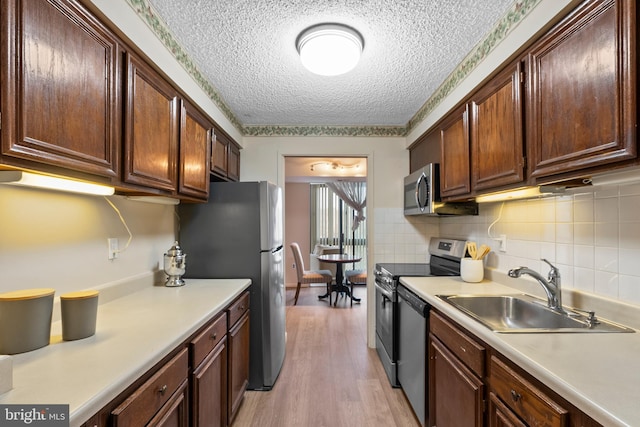 kitchen with sink, light hardwood / wood-style flooring, appliances with stainless steel finishes, backsplash, and a textured ceiling