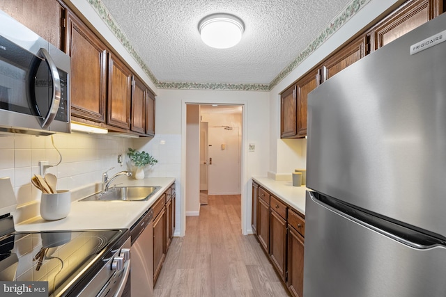 kitchen featuring sink, light wood-type flooring, decorative backsplash, stainless steel appliances, and a textured ceiling