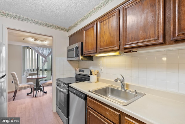 kitchen featuring sink, a textured ceiling, appliances with stainless steel finishes, light hardwood / wood-style floors, and backsplash