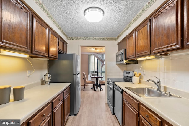 kitchen with appliances with stainless steel finishes, sink, backsplash, a textured ceiling, and light hardwood / wood-style flooring