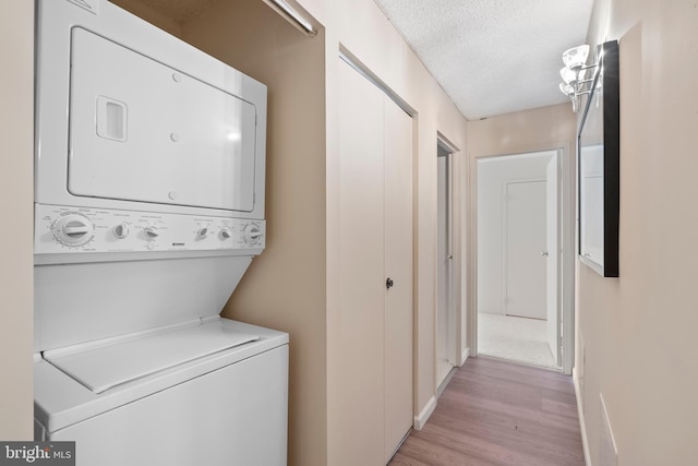 laundry area with light wood-type flooring, a textured ceiling, and stacked washer / dryer