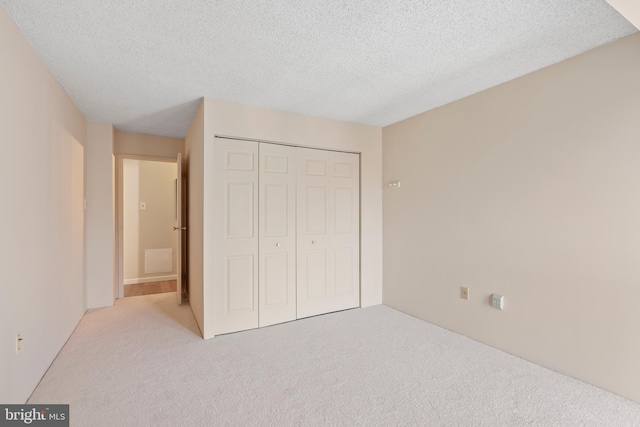 unfurnished bedroom featuring light carpet, a textured ceiling, and a closet