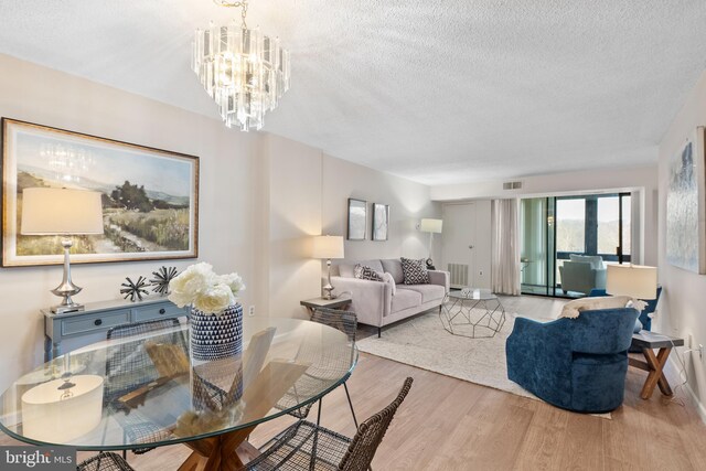 living room with a chandelier, a textured ceiling, and light hardwood / wood-style flooring