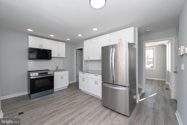 kitchen with white cabinetry, stainless steel appliances, light stone counters, light hardwood / wood-style floors, and decorative backsplash