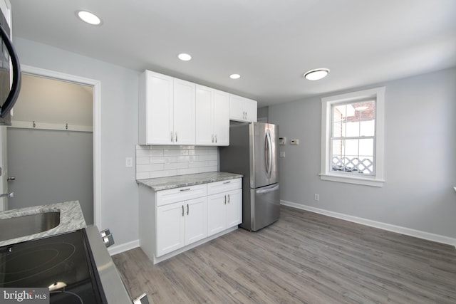 kitchen featuring sink, tasteful backsplash, light stone counters, stainless steel fridge, and white cabinets