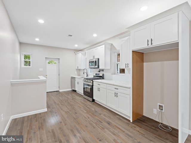 kitchen with white cabinetry, sink, decorative backsplash, stainless steel appliances, and light hardwood / wood-style flooring