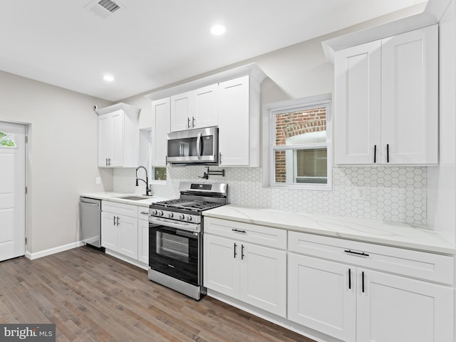 kitchen with appliances with stainless steel finishes, light stone countertops, sink, and white cabinets