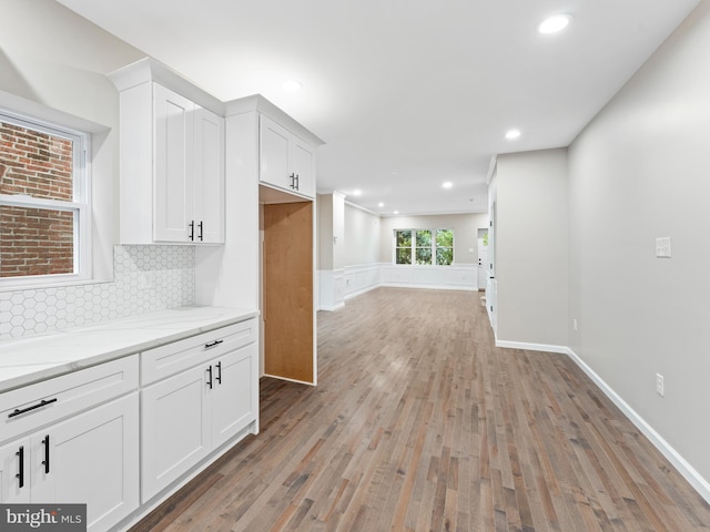 kitchen with decorative backsplash, light stone countertops, light hardwood / wood-style floors, and white cabinets