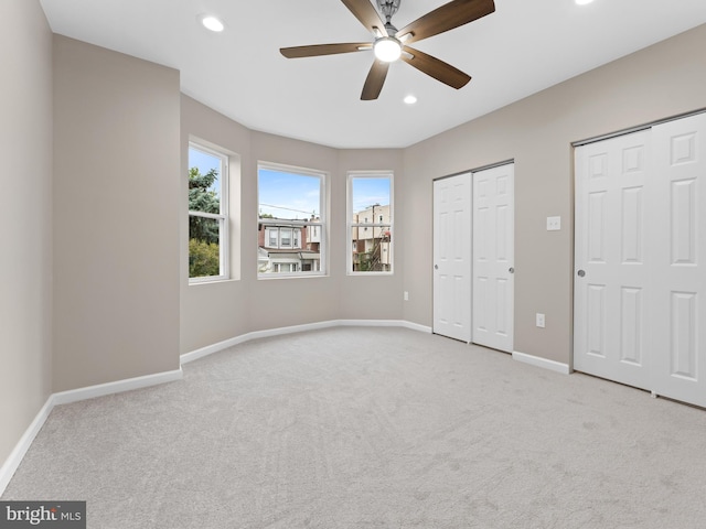 unfurnished bedroom featuring ceiling fan, light carpet, and two closets