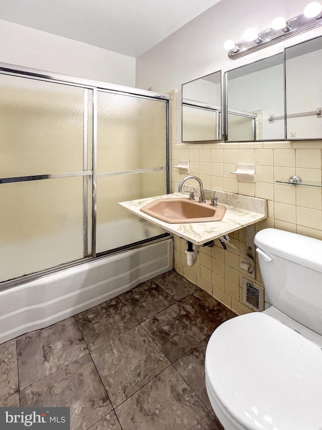 full bathroom featuring combined bath / shower with glass door, tasteful backsplash, sink, tile walls, and toilet