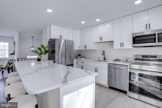 kitchen with pendant lighting, sink, a breakfast bar area, appliances with stainless steel finishes, and light stone counters