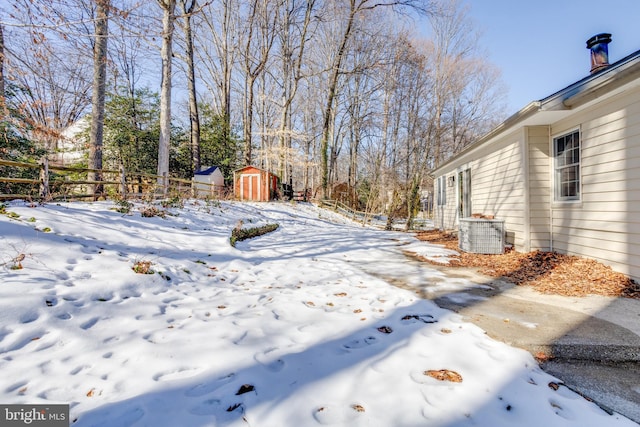 yard covered in snow with cooling unit and a storage shed