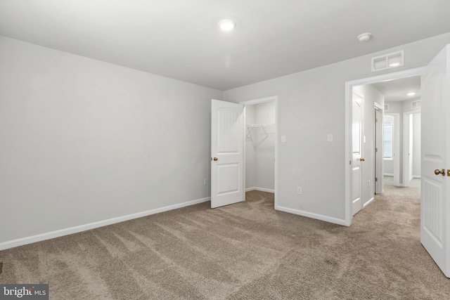 unfurnished bedroom with a walk in closet, light colored carpet, and a closet