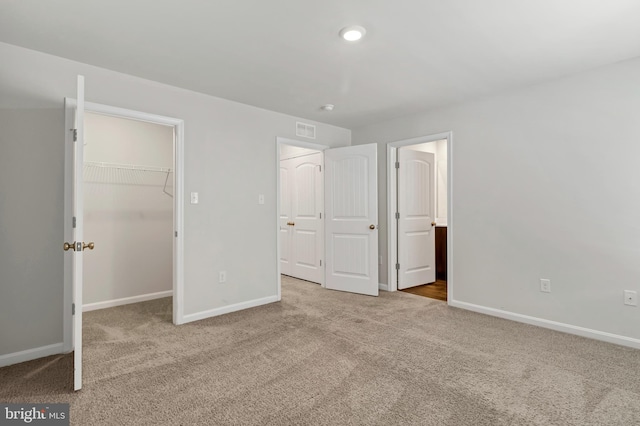 unfurnished bedroom with a walk in closet, light colored carpet, and a closet