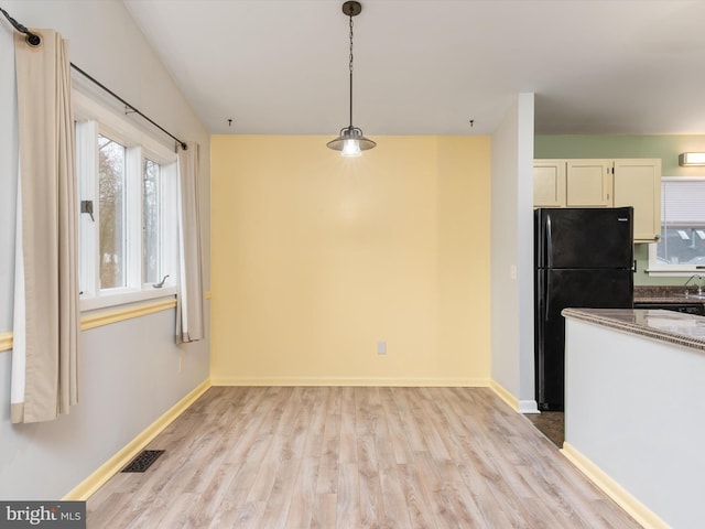 kitchen featuring black refrigerator, decorative light fixtures, light hardwood / wood-style flooring, and dark stone countertops