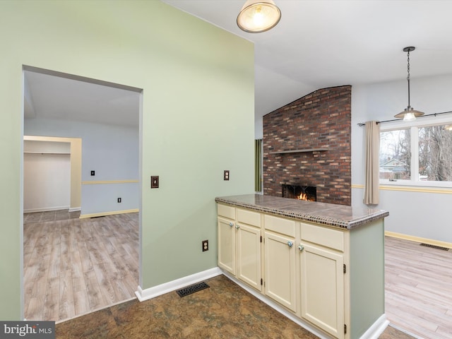 kitchen featuring vaulted ceiling, kitchen peninsula, a brick fireplace, light wood-type flooring, and cream cabinetry