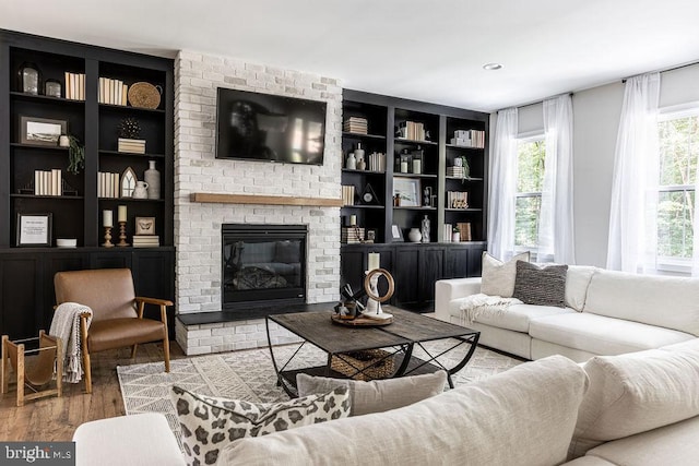 living room with hardwood / wood-style flooring, a brick fireplace, and built in features