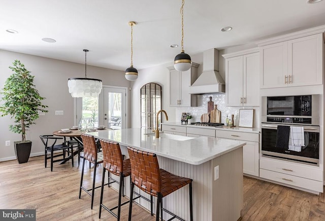 kitchen with appliances with stainless steel finishes, sink, white cabinets, custom exhaust hood, and a kitchen island with sink