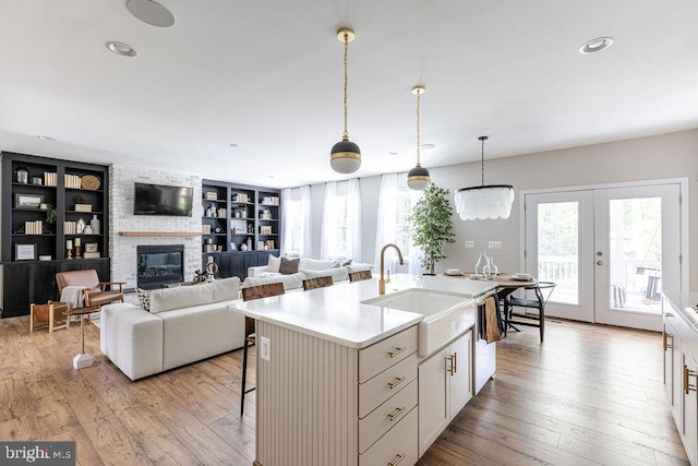 kitchen with sink, an island with sink, built in shelves, decorative light fixtures, and french doors