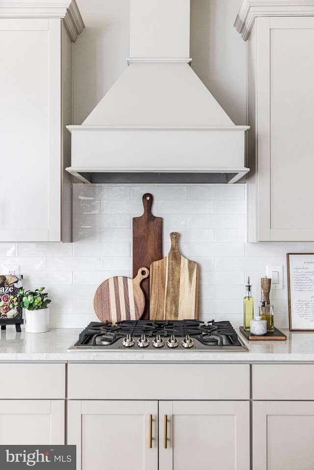 kitchen featuring tasteful backsplash, white cabinetry, custom exhaust hood, and stainless steel gas cooktop