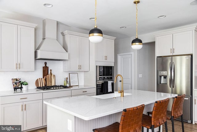 kitchen featuring sink, stainless steel appliances, a center island with sink, decorative light fixtures, and custom exhaust hood