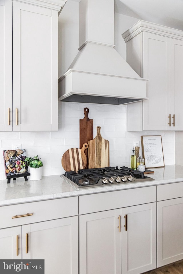 kitchen featuring backsplash, stainless steel gas stovetop, white cabinets, and premium range hood