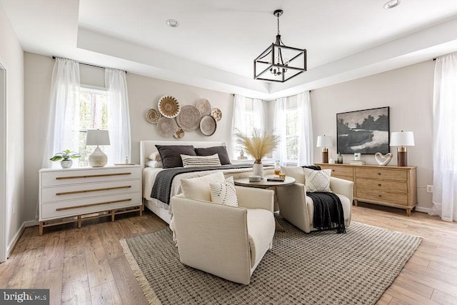 bedroom featuring an inviting chandelier, wood-type flooring, and a tray ceiling