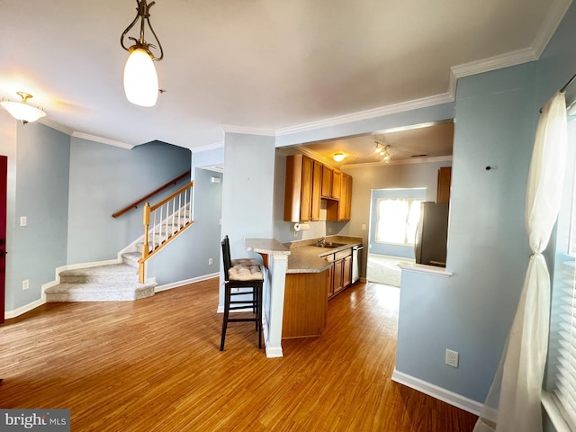 kitchen featuring pendant lighting, sink, stainless steel dishwasher, crown molding, and light wood-type flooring