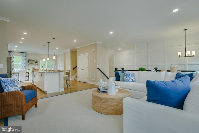 living room featuring sink, a notable chandelier, ornamental molding, and light wood-type flooring