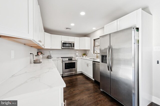 kitchen featuring sink, white cabinets, dark hardwood / wood-style flooring, light stone counters, and stainless steel appliances