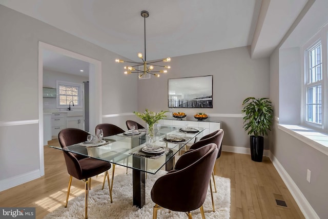 dining space with an inviting chandelier, sink, light hardwood / wood-style flooring, and a wealth of natural light