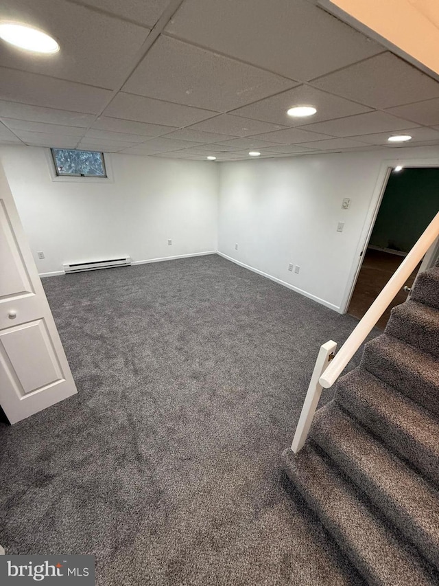 basement featuring baseboard heating, a paneled ceiling, and dark carpet