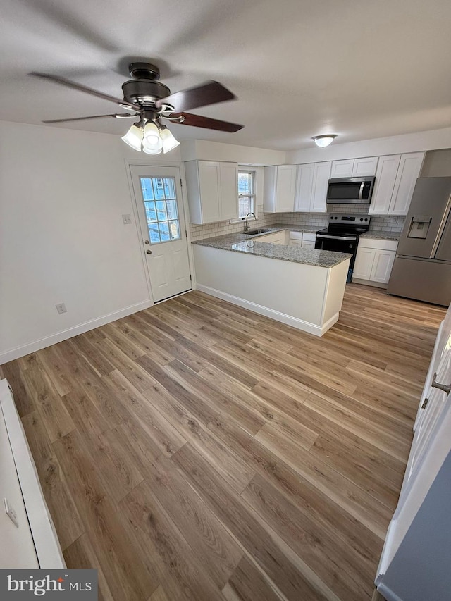 kitchen with sink, appliances with stainless steel finishes, white cabinetry, decorative backsplash, and kitchen peninsula