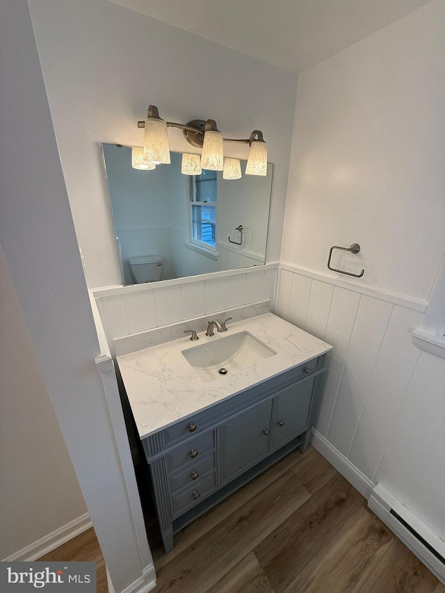 bathroom with vanity, hardwood / wood-style floors, baseboard heating, and toilet