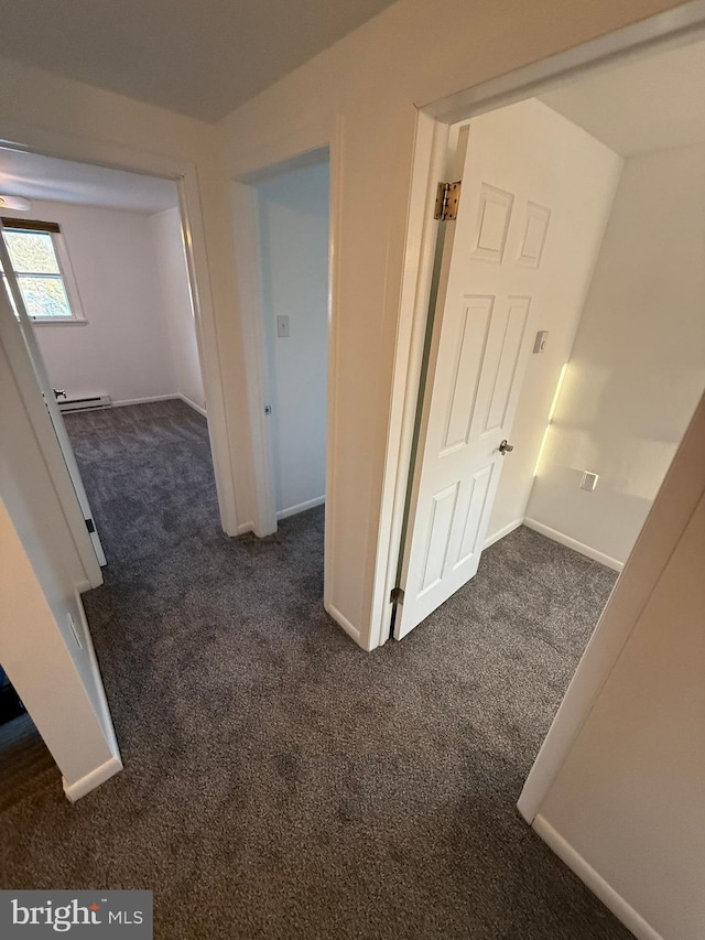 corridor with dark carpet and a baseboard heating unit