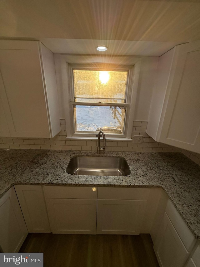 kitchen with light stone countertops, sink, white cabinets, and backsplash