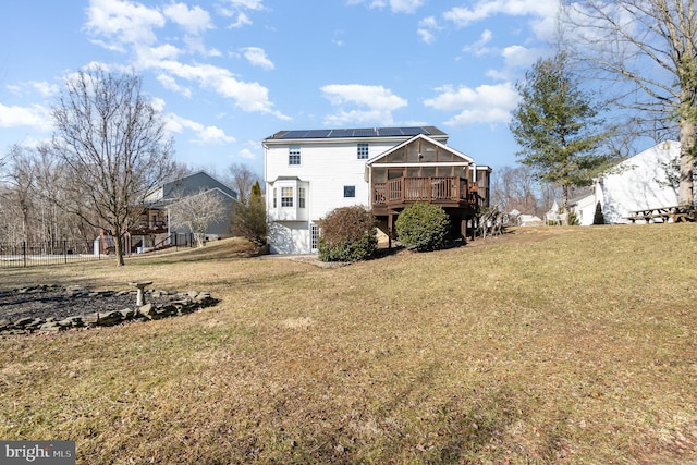 rear view of house featuring a wooden deck, a yard, and solar panels