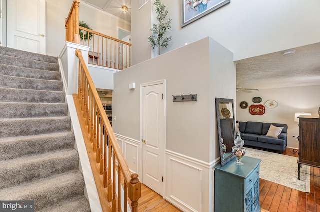 stairs with ceiling fan, hardwood / wood-style floors, a textured ceiling, and a high ceiling